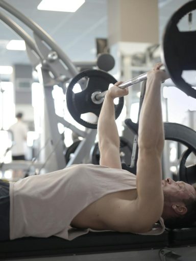 Adult man performing bench press in a gym, focusing on strength and fitness.