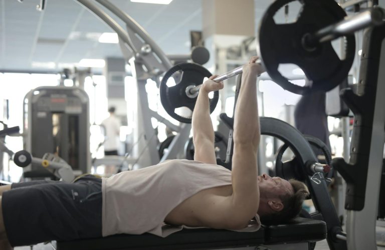Adult man performing bench press in a gym, focusing on strength and fitness.